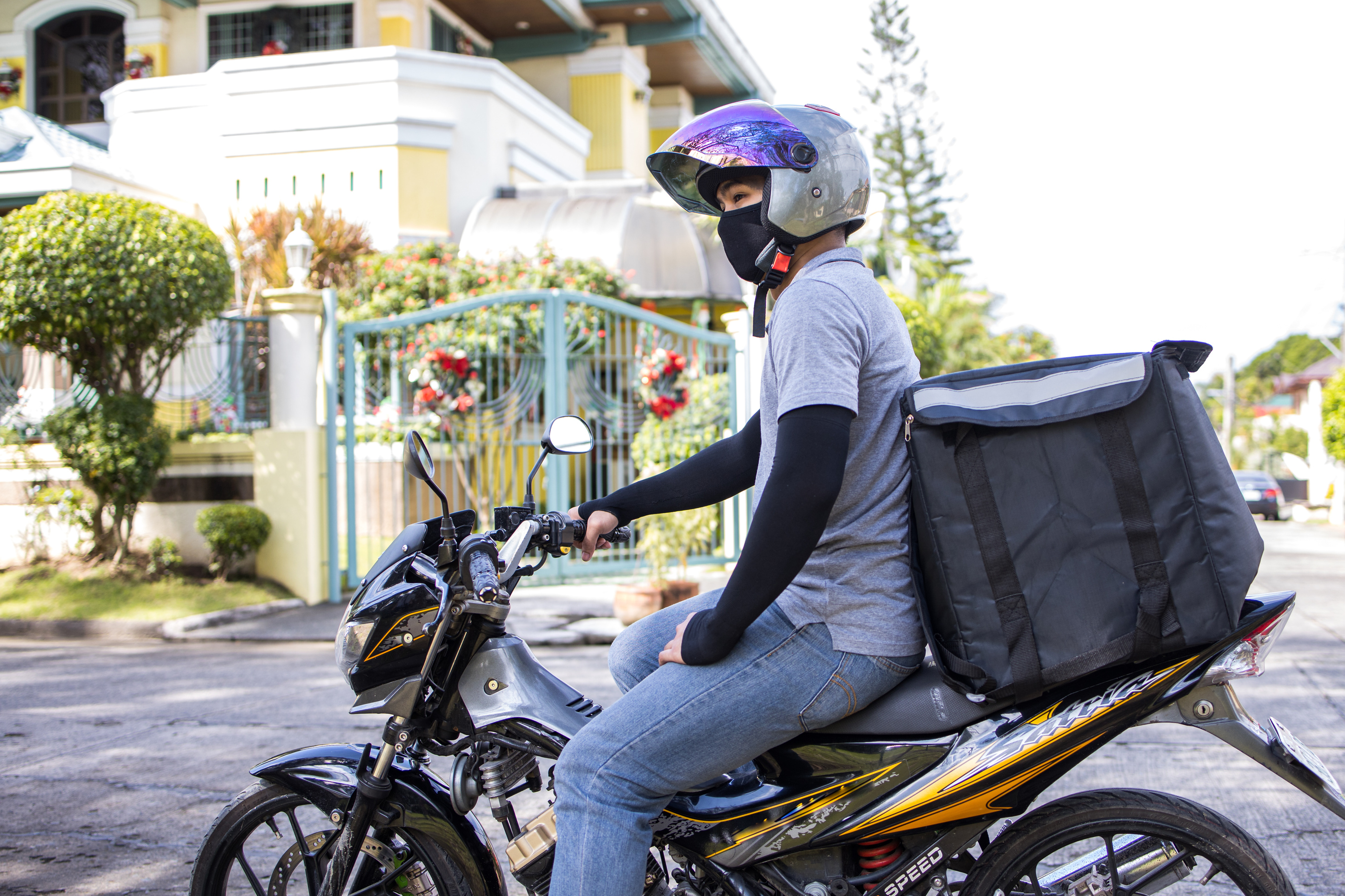 Deliveryman in Face Mask Sitting and Waiting on Motorcycle Outdoor